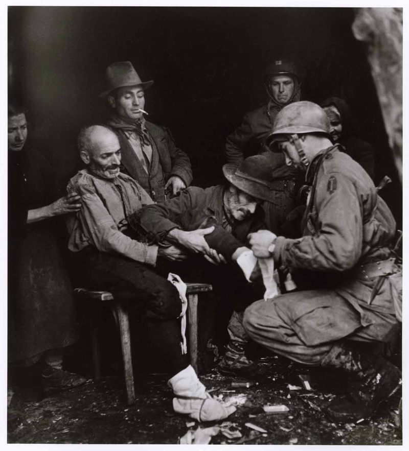 Az amerikai-kanadai egyesített speciális katonai csapat katonája sebesült civilt lát el. A pásztor lábát Domenico Matteo tartja. Radicosa, Cassino közelében, 1944. január 4. Fényképezte Robert Capa © International Center of Photography, New York – Magyar Nemzeti Múzeum gyűjteménye